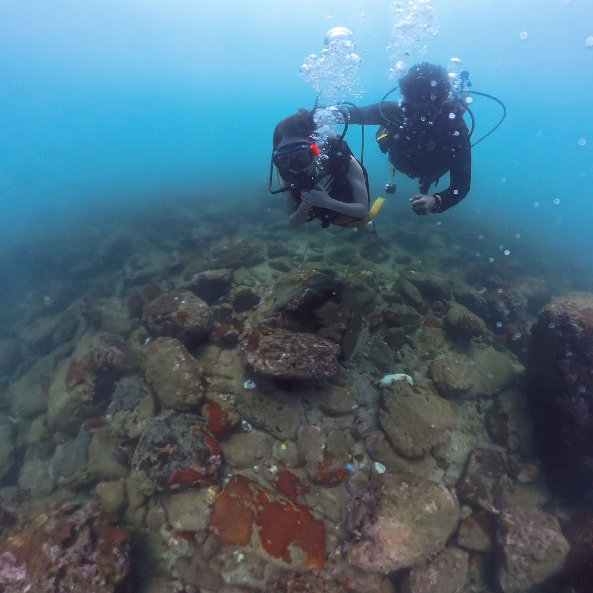 Scuba instructor guiding a diver over a rocky reef underwater